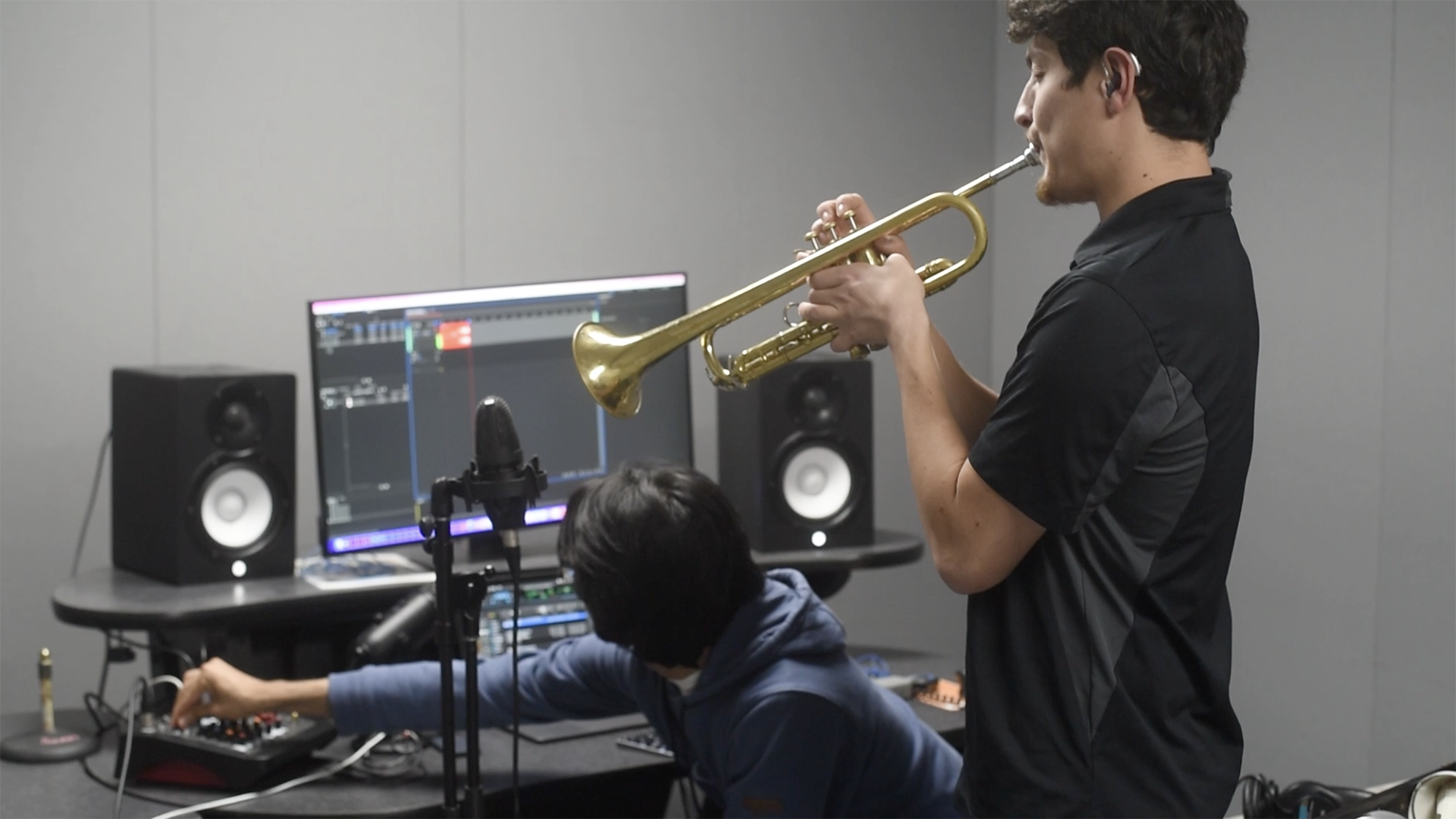Daniel Sarch plays the trumpet as a fellow student edits on a computer.